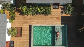 Vista aérea de un área de piscina con una persona nadando, rodeada de madera y follaje.