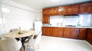 Une cuisine avec des meubles de rangement en bois, une table de salle à manger ronde entourée de chaises et un réfrigérateur.