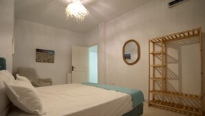 Une chambre à coucher comprenant un lit, une chaise, une armoire en bois et une porte donnant sur une autre pièce.