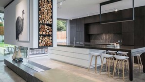 Een moderne keuken met een centraal kookeiland, barstoelen en een groot raam.
