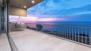 Een balkon met uitzicht op zee, een hangstoel en een metalen hekwerk.