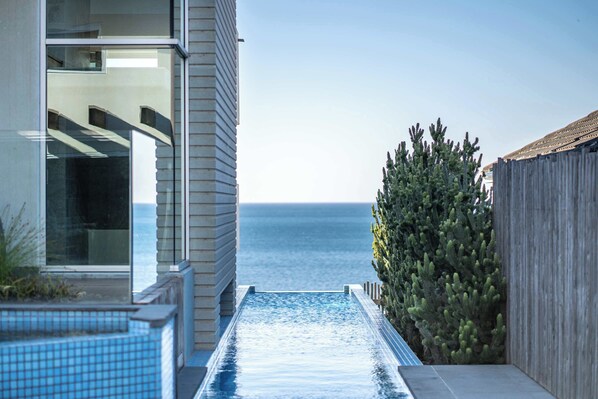 A modern building with a glass facade, a pool, and a view of the sea.