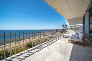 A balcony with a view of the beach, a sofa, and a railing. - One Eighty Marino (Marino)