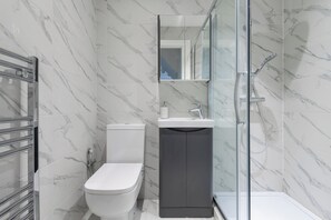 A modern bathroom with a toilet, sink, and glass shower enclosure. - A wonderful and spacious house in a charming road (Greater London)