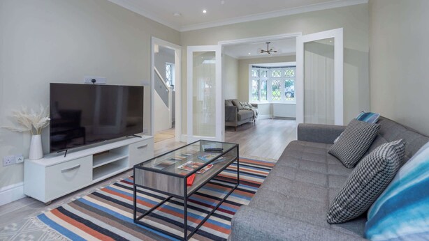 Una sala de estar moderna con un televisor de pantalla plana, una mesa de centro de vidrio, un sofá gris y un tapete a rayas.