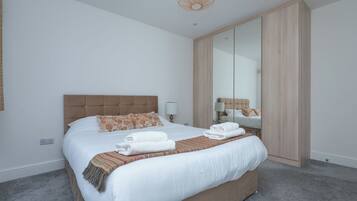 A hotel room with a large bed, a wardrobe, a mirror, and a hanging light fixture.