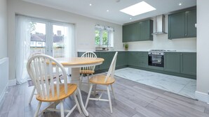 A modern kitchen with green cabinets, a dining table with chairs, and a skylight. - A wonderful and spacious house in a charming road (Greater London)