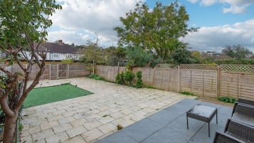 A backyard with a paved patio, a small lawn, and a wooden fence.