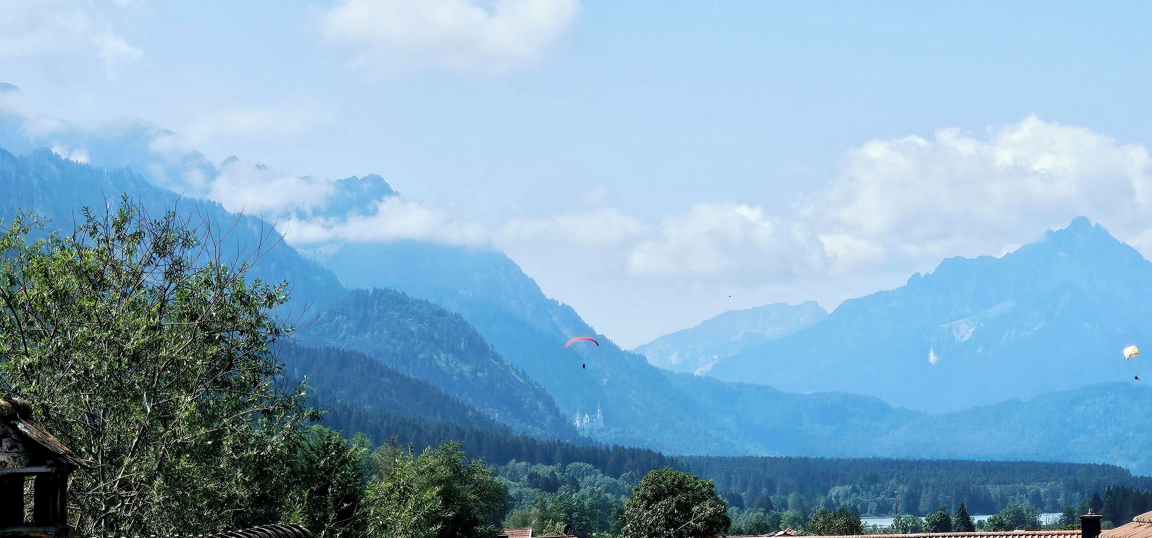 A mountainous landscape with a clear sky and a person paragliding.