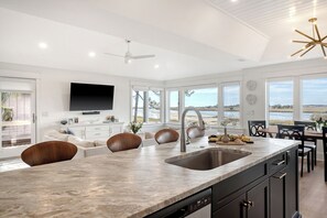 A modern kitchen with a large island, built-in appliances, and a view of the beach.