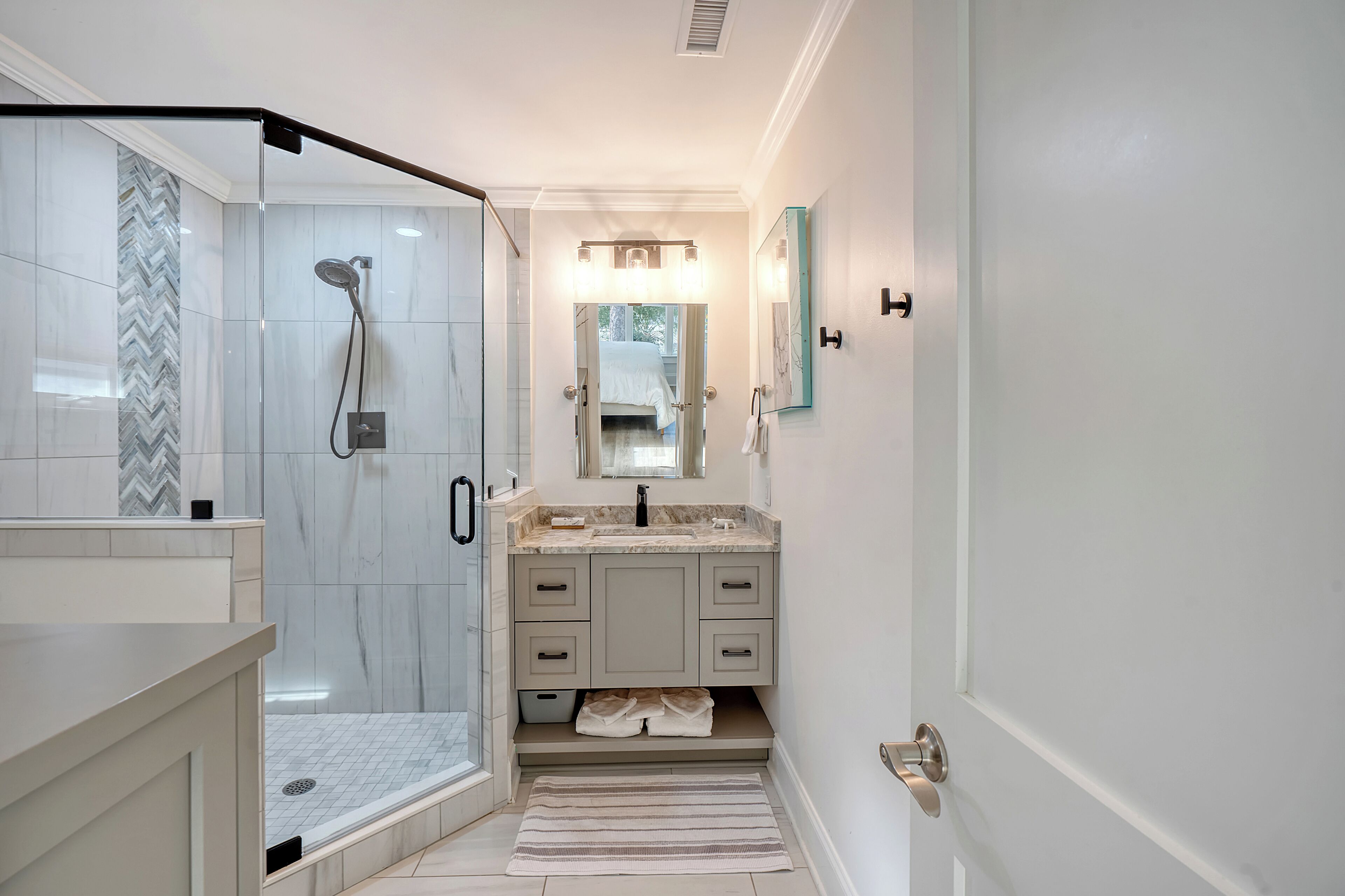 A modern bathroom with a glass-enclosed shower, a vanity with a mirror, and a herringbone-patterned tile backsplash.
