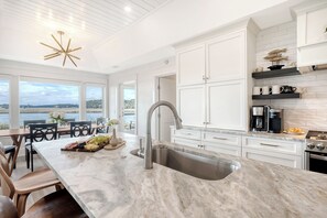 A modern kitchen with a large island, stainless steel sink, and white cabinetry.