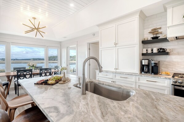 A modern kitchen with a large island, stainless steel sink, and white cabinetry.