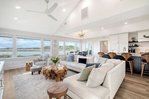 A spacious living room with a large window overlooking a body of water, a white sofa, a coffee table, and a wooden coffee table.