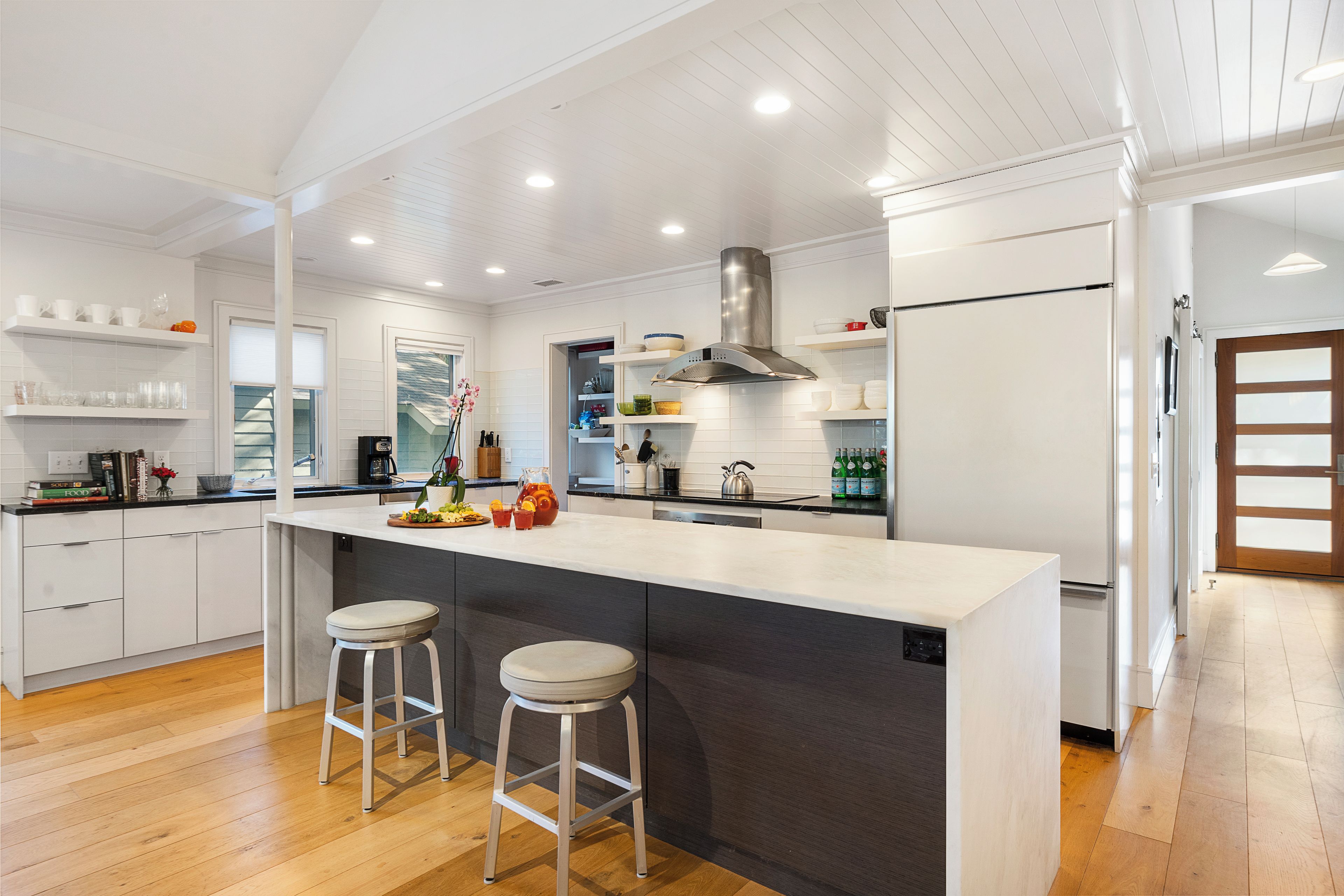 A modern kitchen with white cabinetry, a stainless steel range hood, and a large island with bar stools.