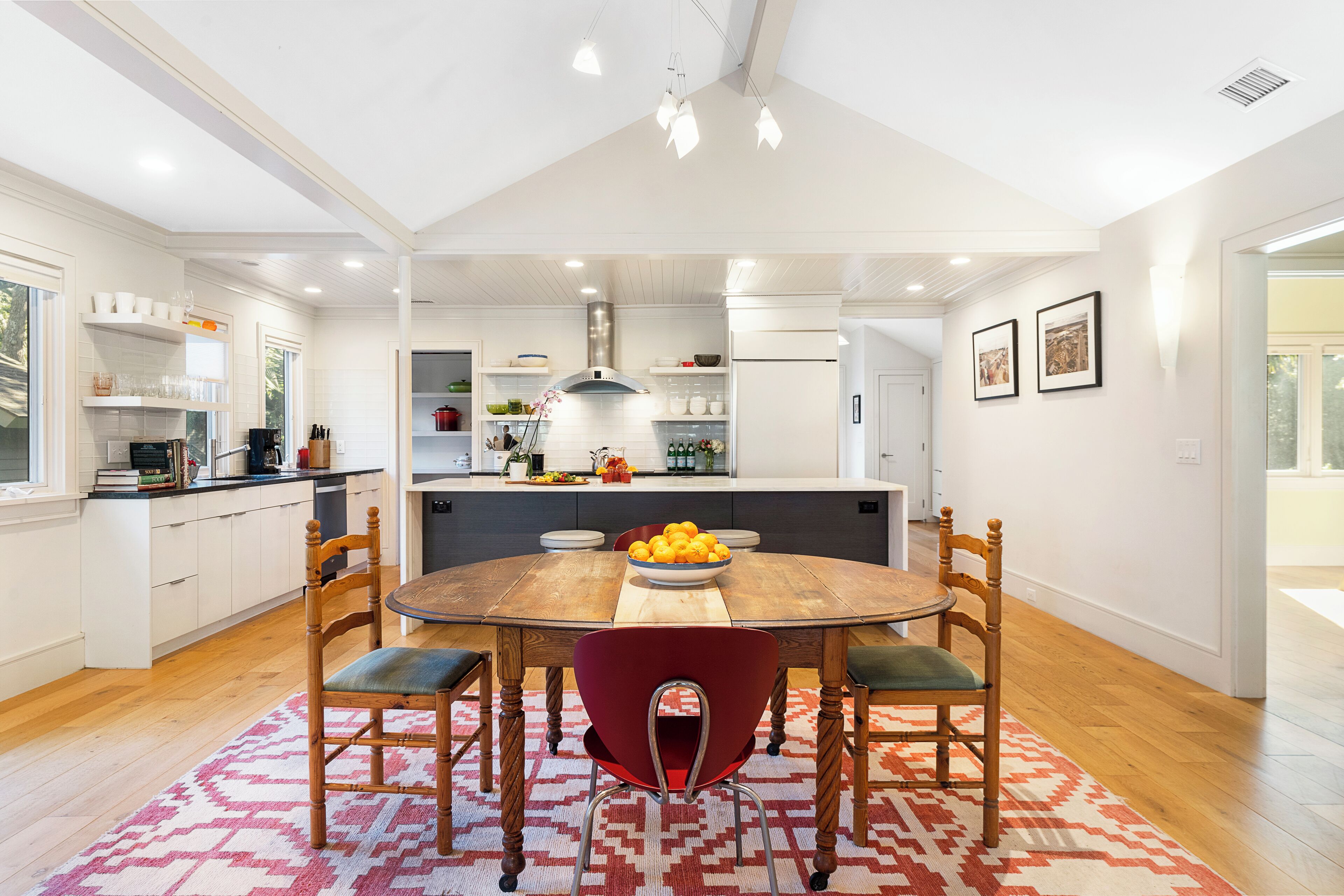 A modern kitchen with white cabinets, a wooden dining table, and a red chair.