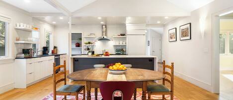 A modern kitchen with white cabinets, a wooden dining table, and a red chair.