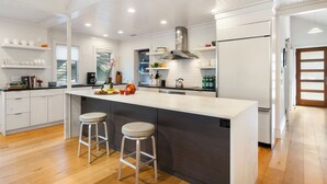 A modern kitchen with white cabinetry, a stainless steel range hood, and a large island with bar stools. - Yards to the beach, stunning new reno (Kiawah Island)