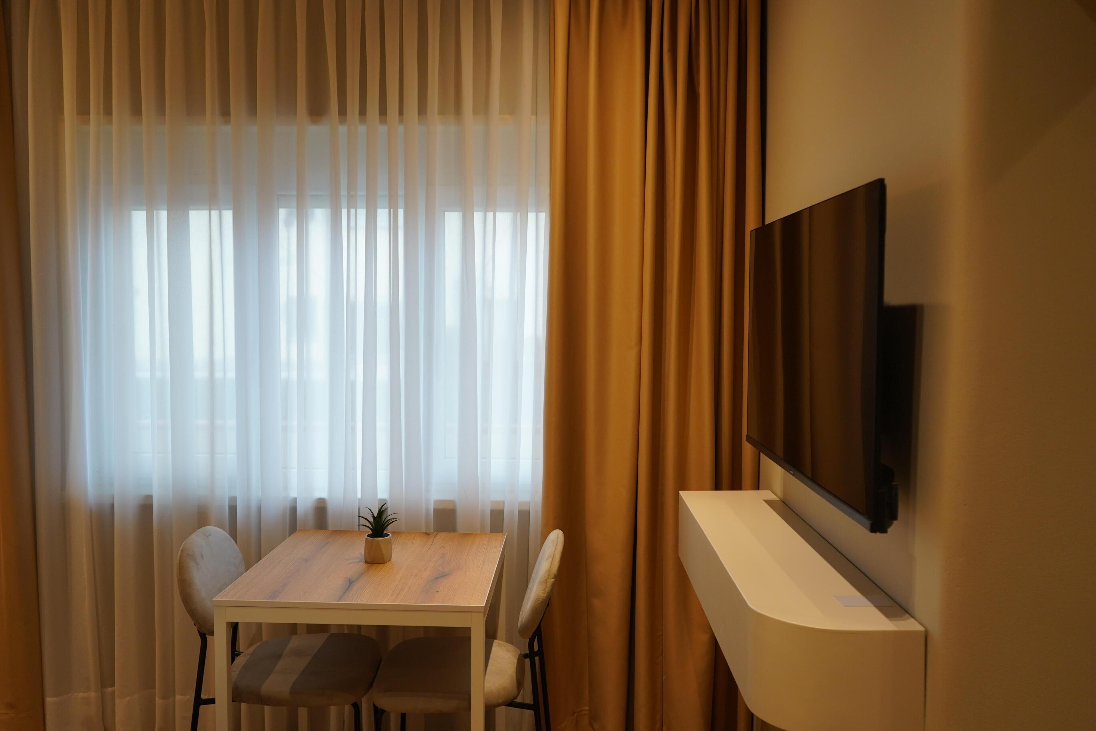 A modern room with a wooden table, two chairs, a small potted plant, and a mounted TV.