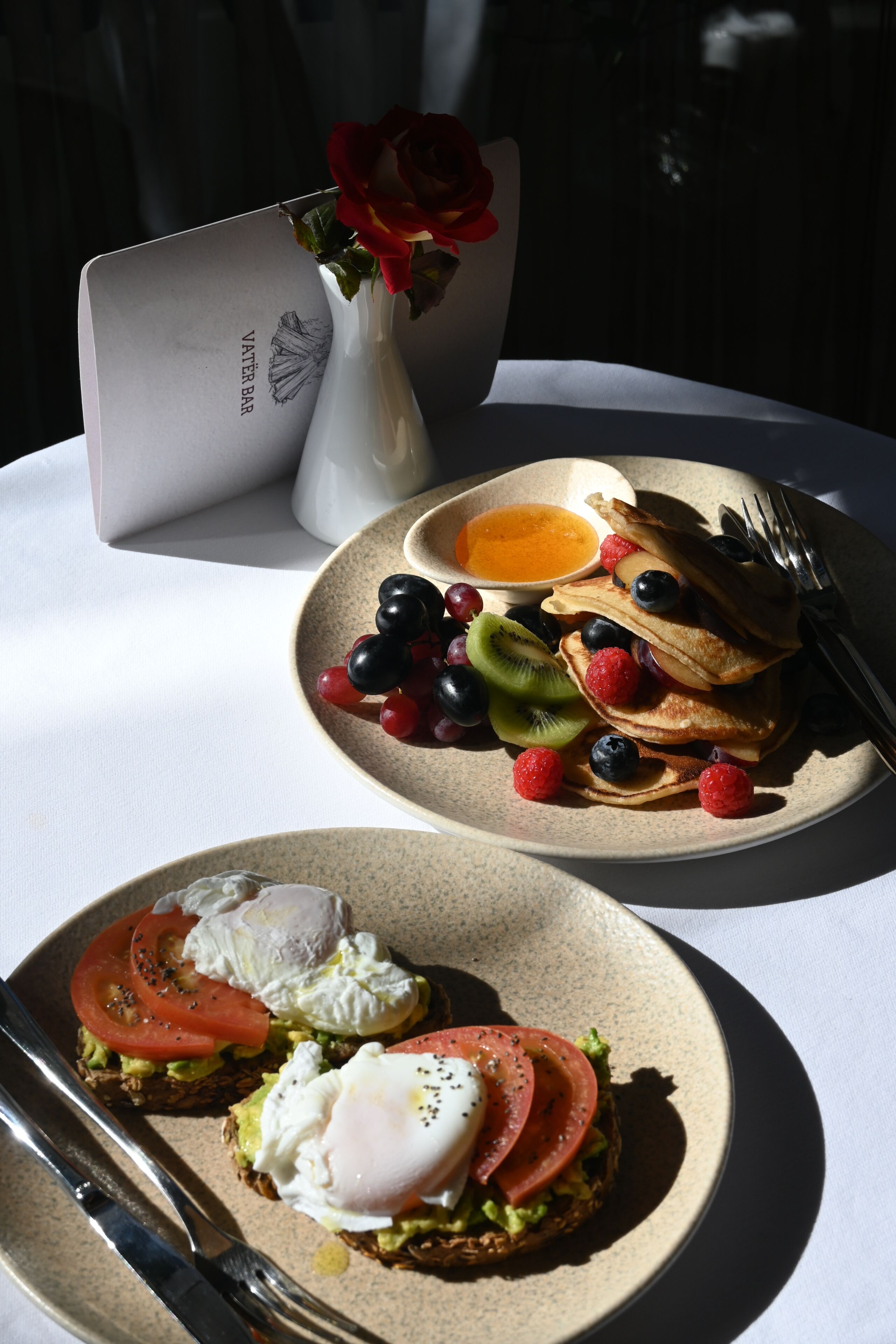A breakfast setting with pancakes, berries, and a small vase with a rose.