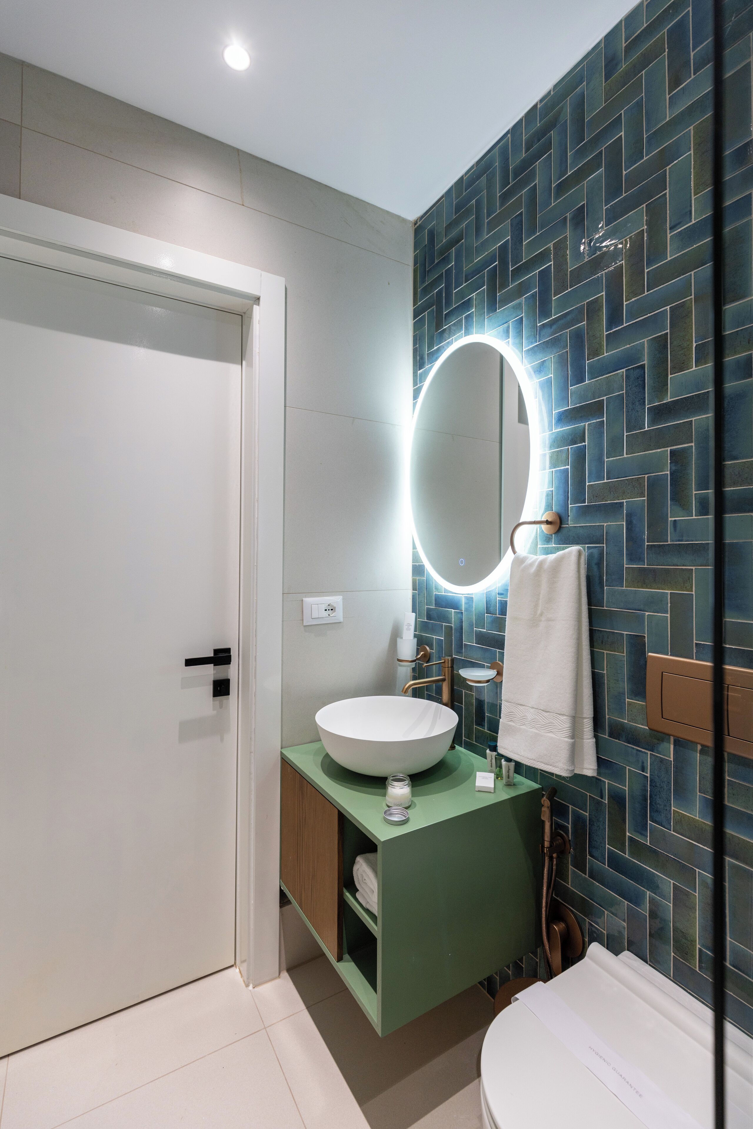 Ein modernes Badezimmer mit einem weißen Waschbecken, einem grünen Waschtischunterschrank und einer Rückwand mit Fischgrätmuster.