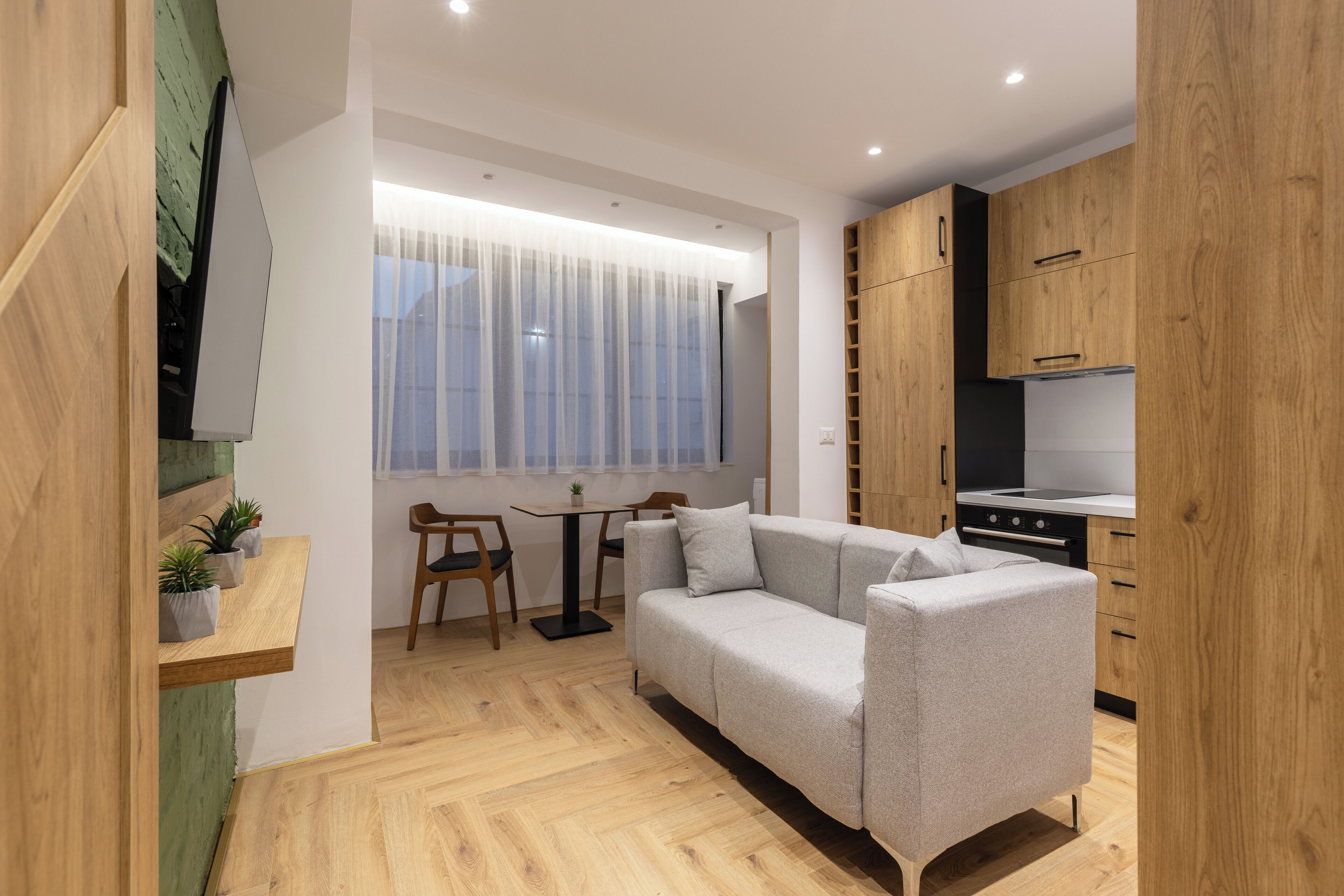 Un salon moderne avec un canapé gris, un plancher en bois et un petit coin repas comprenant une table et des chaises.