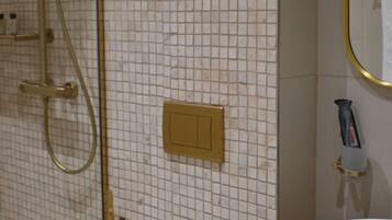 Une salle de bain avec un lavabo blanc, une douche dorée et un miroir avec un cadre doré.