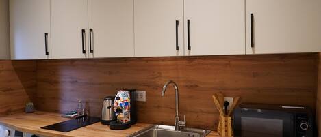 Una cocina con gabinetes blancos, una encimera de madera, un lavamanos, una cafetera, un tostador y una lavadora.