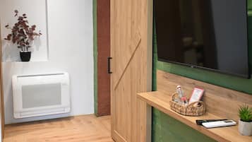 A room with a wooden cabinet, a mounted TV, a small shelf with a plant, a basket with a bottle, and a remote control.