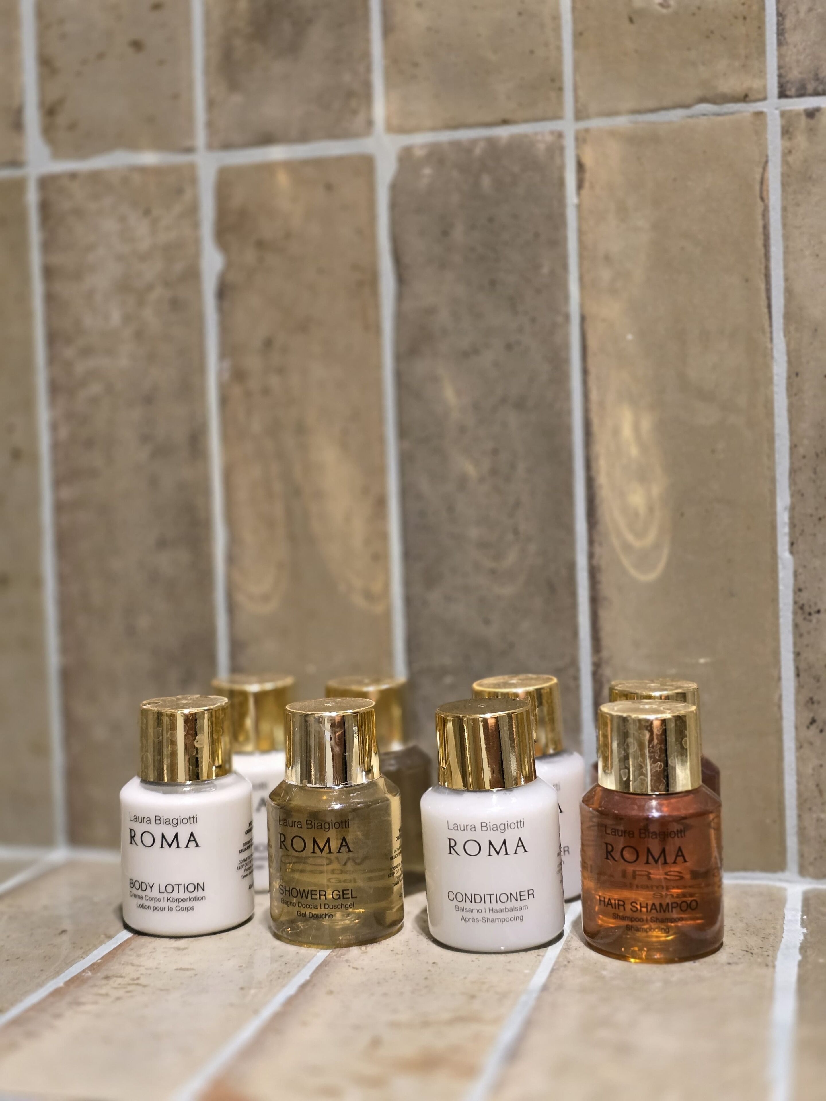 Ein Badezimmer mit Fliesenwand und Ablagefläche mit verschiedenen Laura Biagiotti ROMA Produkten.