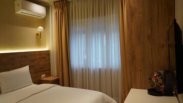 Une chambre d’hôtel comprenant un lit, une table de chevet, une lampe, un appareil de climatisation, des rideaux et un téléviseur.