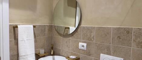 A bathroom with a white sink, a round mirror, a towel rack, a soap dispenser, and a light switch.