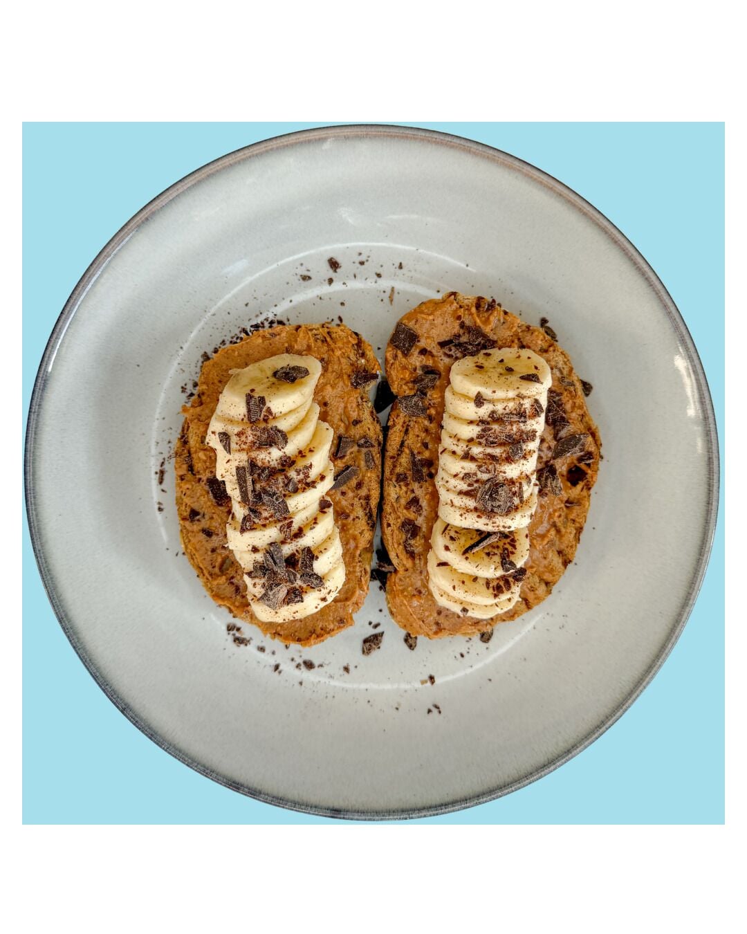 Um prato com duas porções de comida cobertas com fatias de banana e raspas de chocolate.