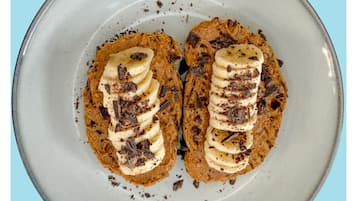 Um prato com duas porções de comida cobertas com fatias de banana e raspas de chocolate.