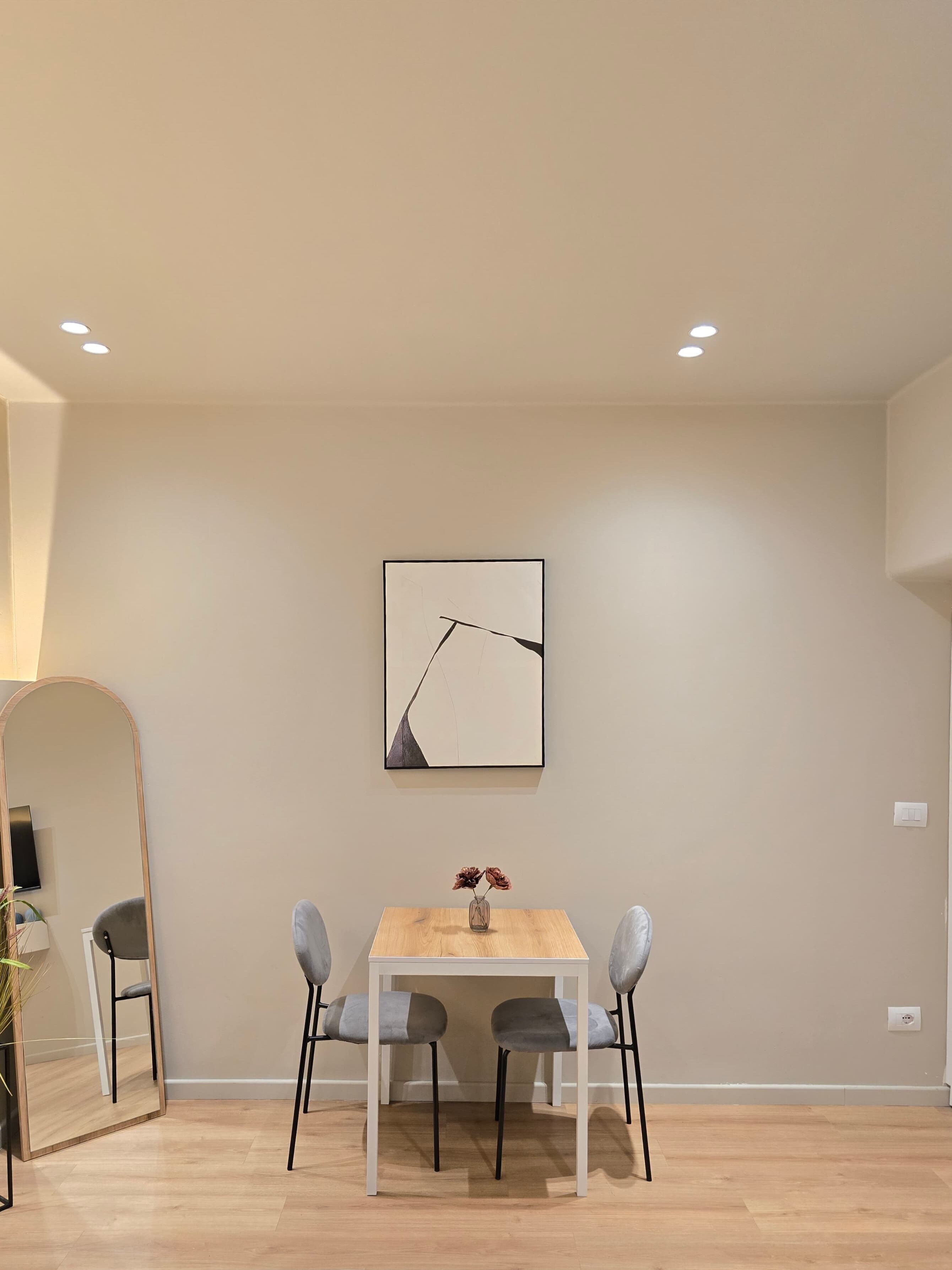 Un coin repas minimaliste avec une table en bois, deux chaises grises à revêtement rembourré et un tableau abstrait encadré accroché au mur.