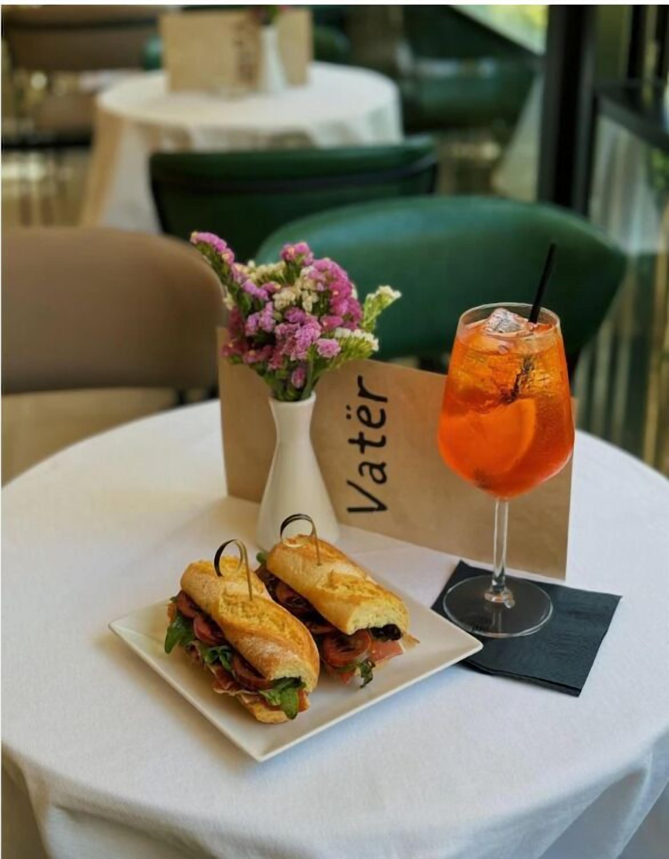 A table with a sandwich, a drink, and a vase of flowers.