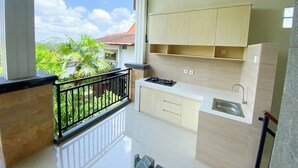 A modern kitchen with light wood cabinets, a stainless steel sink, and a balcony with a black railing. - Oemah Surya Ubud (Ubud)