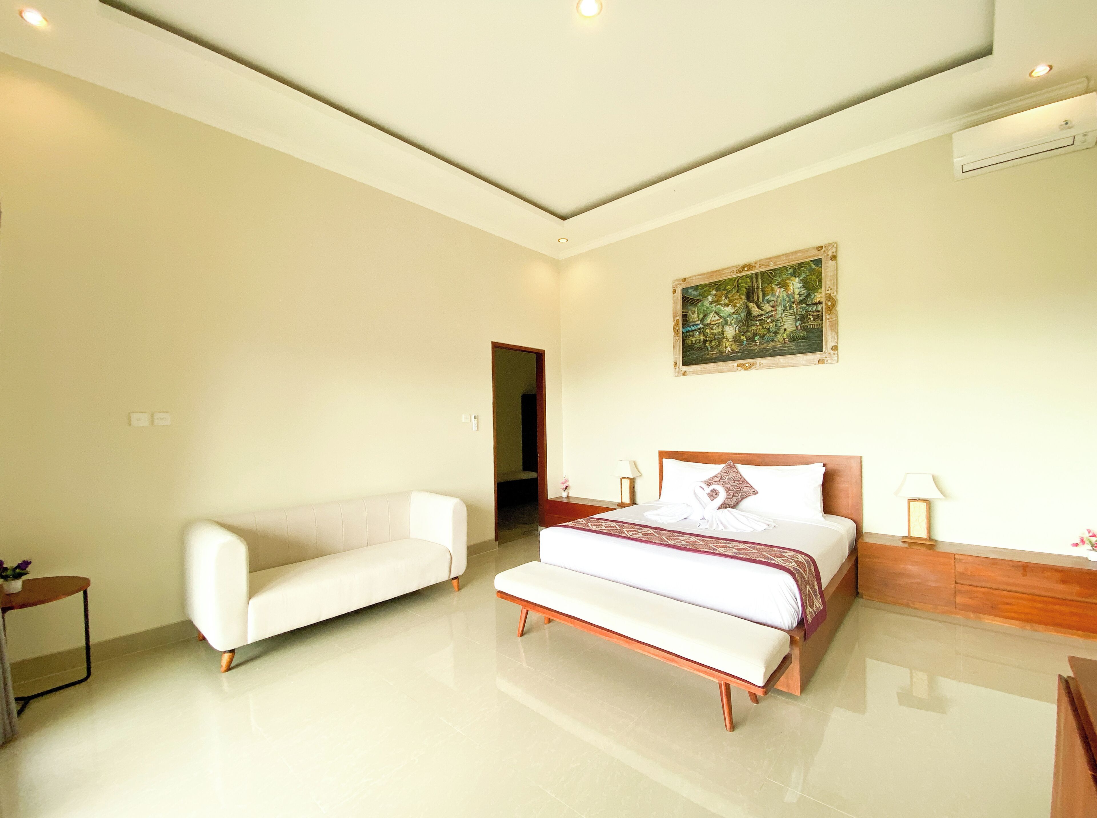 Um quarto espaçoso com uma cama grande, um sofá branco e um banco.