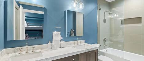 A modern bathroom with a blue accent wall, a large mirror, a double sink vanity, and a glass-enclosed shower area.