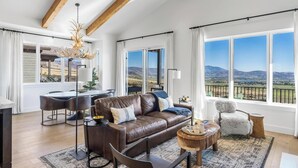 Una sala de estar amplia con un sofá de cuero, una zona de comedor con mesa y sillas, y ventanas grandes con vistas a la montaña.
