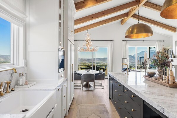A modern kitchen with a large island, a dining area with a view, and a chandelier.