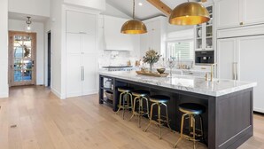 Una cocina moderna con armarios blancos, una isla de mármol con taburetes e iluminación colgante.