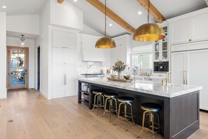 A modern kitchen with white cabinets, a marble island with stools, and pendant lighting.