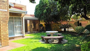 A backyard with a brick house, a covered patio, and a stone table with benches. - Mosele wa Pula Guesthouse  (Rustenburg)