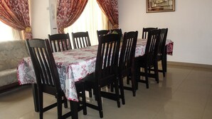 A dining area with a table set for six, surrounded by wooden chairs, with a sofa and curtains in the background. - Mosele wa Pula Guesthouse  (Rustenburg)