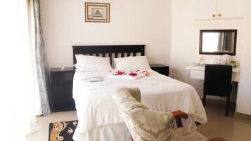 A hotel room with a bed, a desk, a chair, a small table, a mirror, and a picture on the wall.