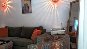 Een woonkamer met een bank, een gestreept fauteuil, een klein wit bijzettafeltje en een wandlamp.