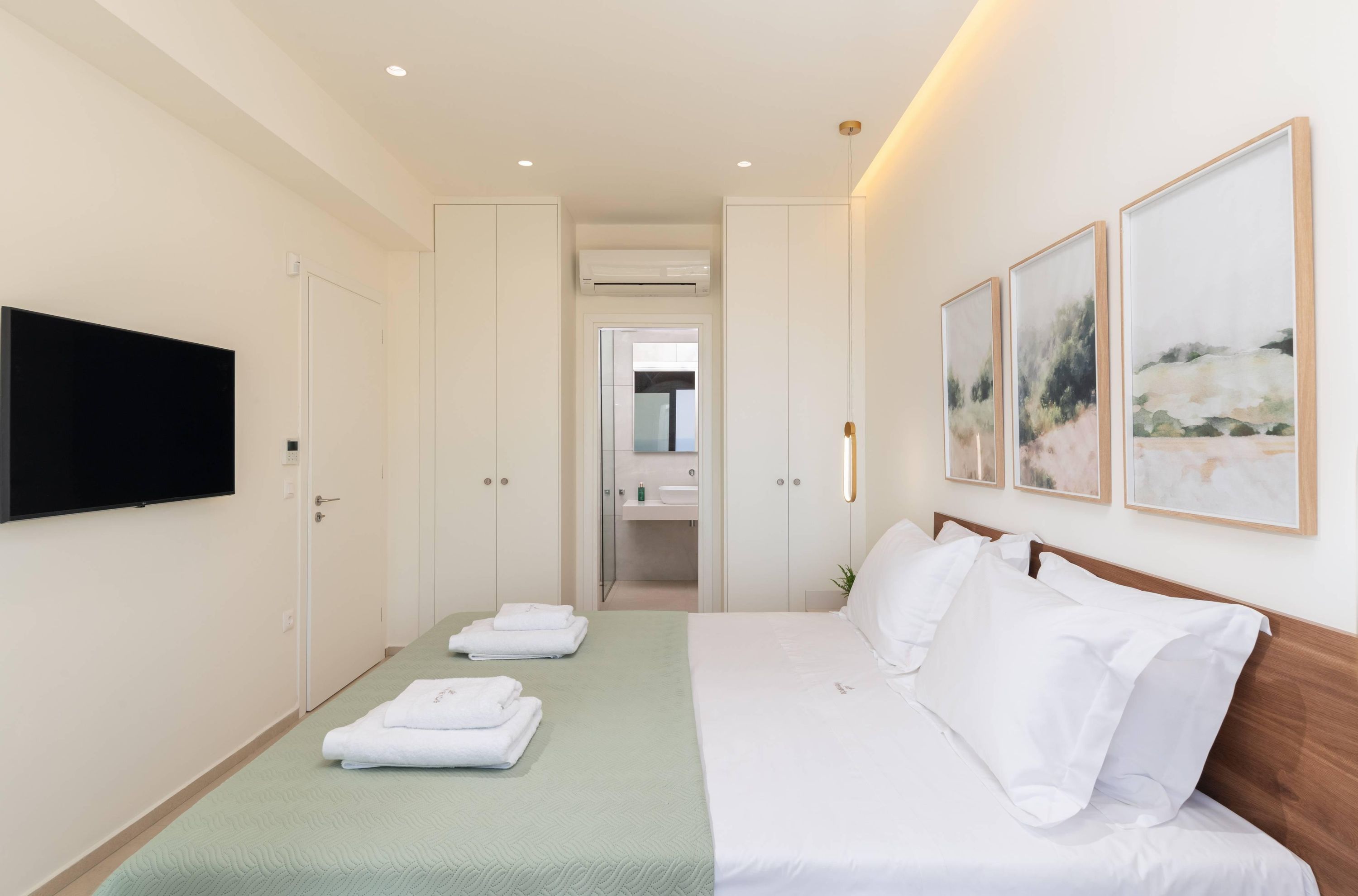 A hotel room with a bed, a TV, a wardrobe, and artwork on the wall.
