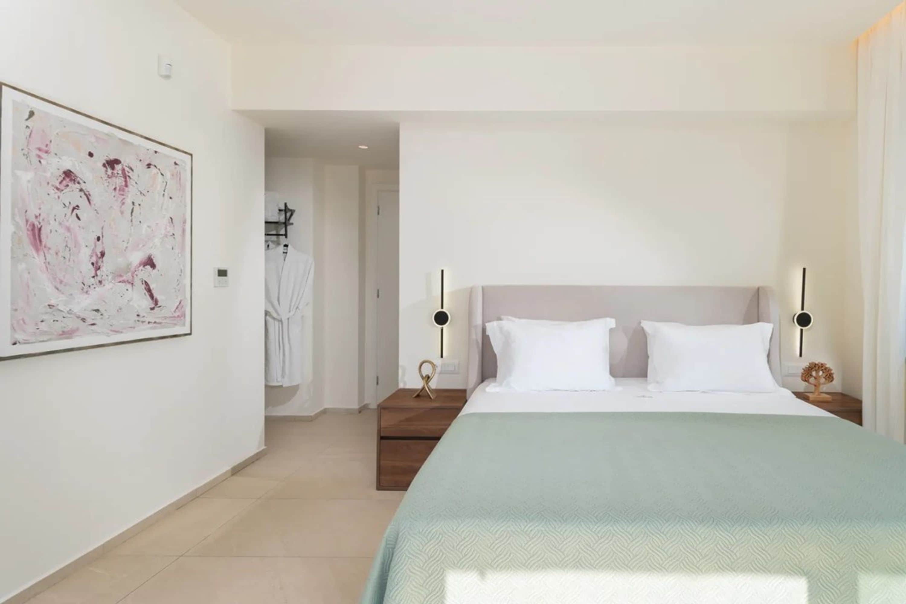 Une chambre d’hôtel moderne dotée d’un grand lit, d’une table de chevet, d’une œuvre d’art accrochée au mur et d’une salle de bain visible.
