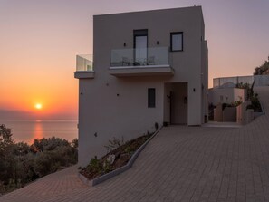 A modern two-story building with a balcony overlooking a body of water during sunset.